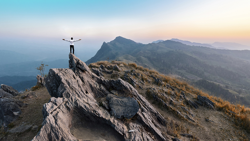 businessman hike on the peak of rocks mountain at sunset, succes